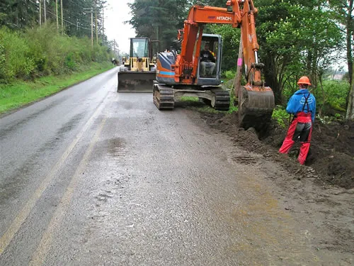A man is working on a road with a backhoe.