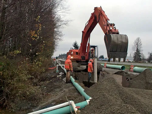 A construction worker is standing in a hole with a red excavator.