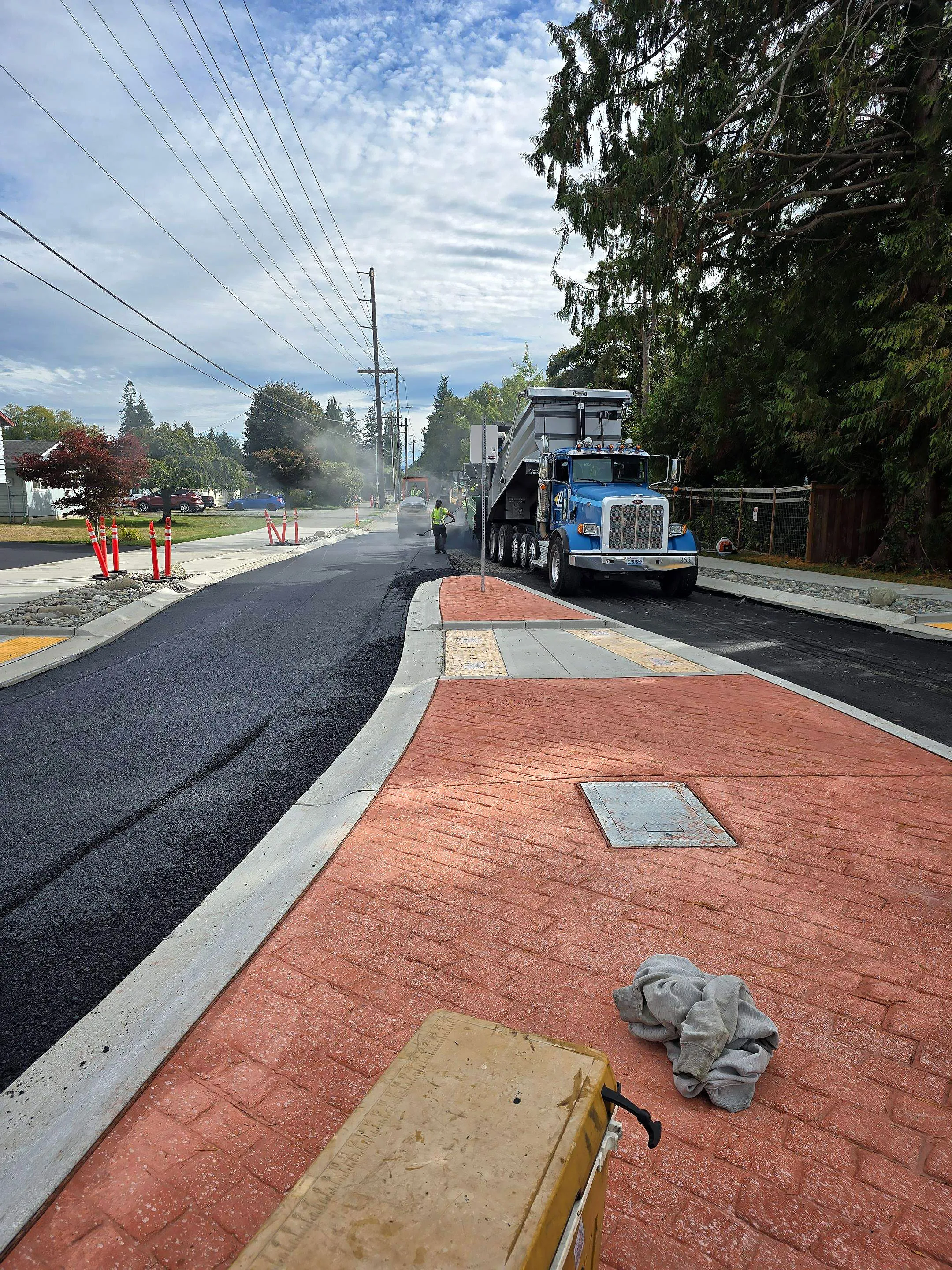 A road is being repaired with a large truck and a man standing on the side of the road.