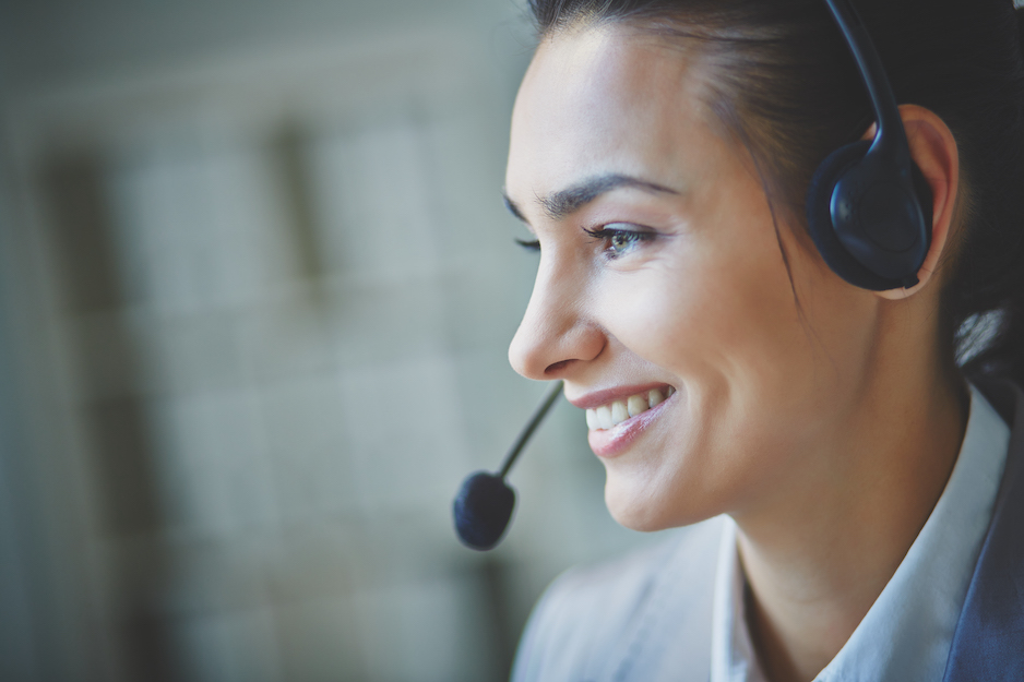 Smiling woman wearing a headset and speaking, with a blurred background.