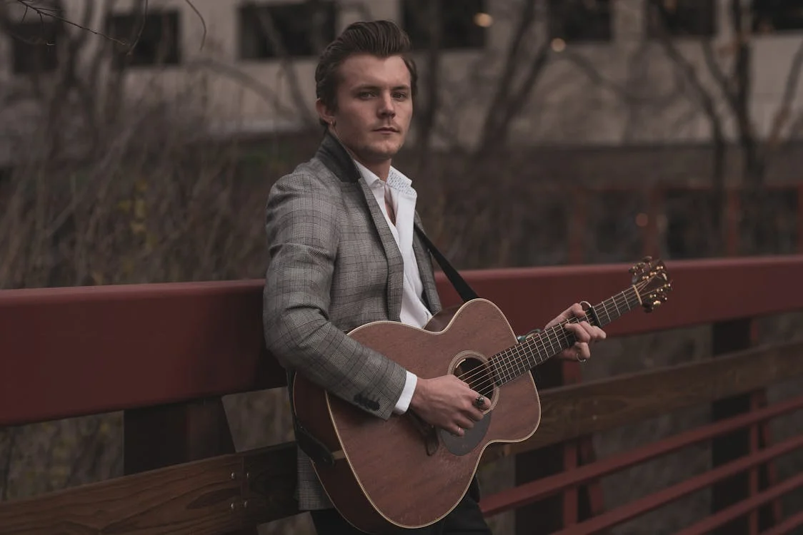 Guitar player, male, in his 30's holding a guitar outside standing in a bridge. 