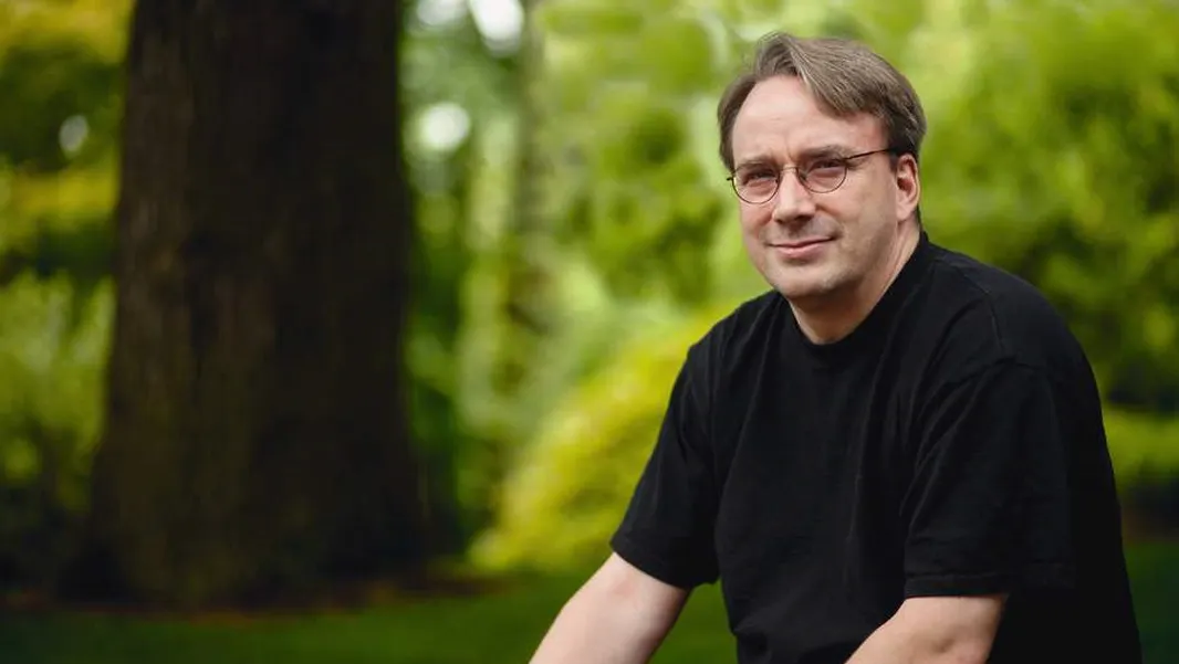 A man in wire-rimmed glasses and a black T-shirt photographed outdoors among trees.