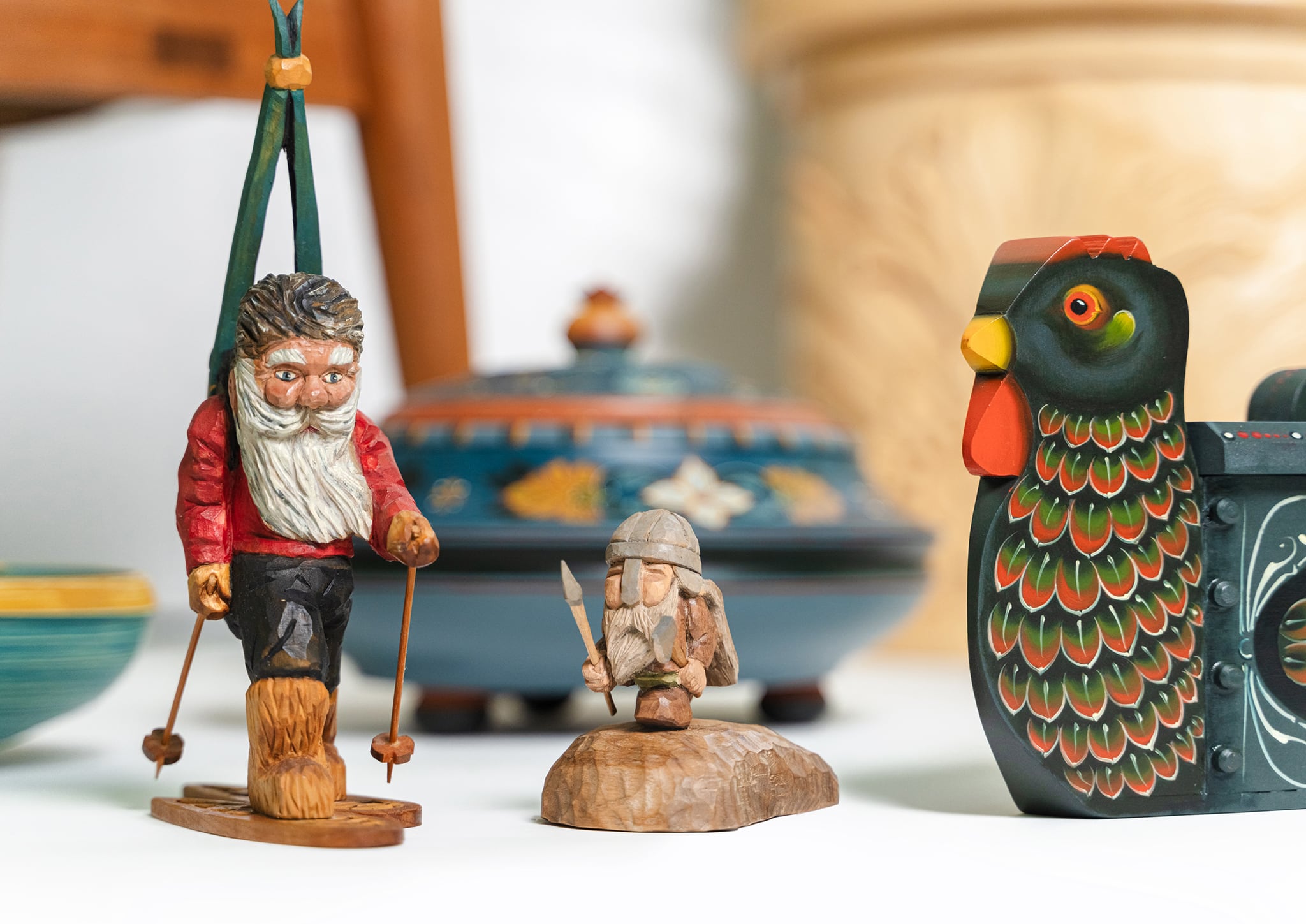Carved and painted Nordic folk-art pieces: a bearded figure on skis, a small Viking figure, a painted bird box and a rosemaled bowl.