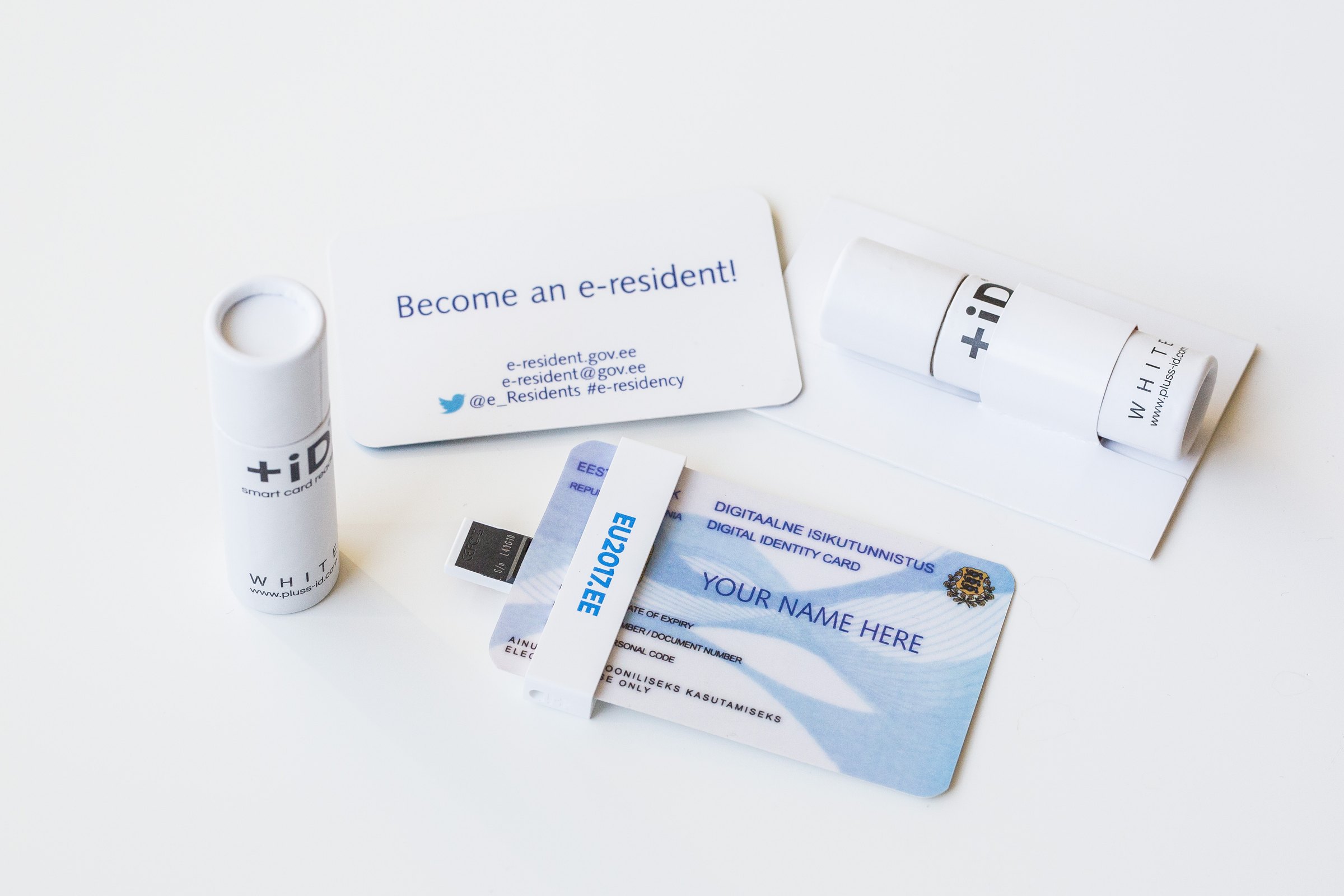 An Estonian ID-card reader beside a promotional e-Residency card printed with the words YOUR NAME HERE, part of a gift set from Estonia's 2017 EU Council presidency.