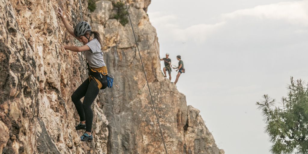Una persona che si arrampica su una ripida parete rocciosa con altre persone sullo sfondo.