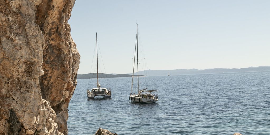 Person rappels down a cliff face above clear blue water.