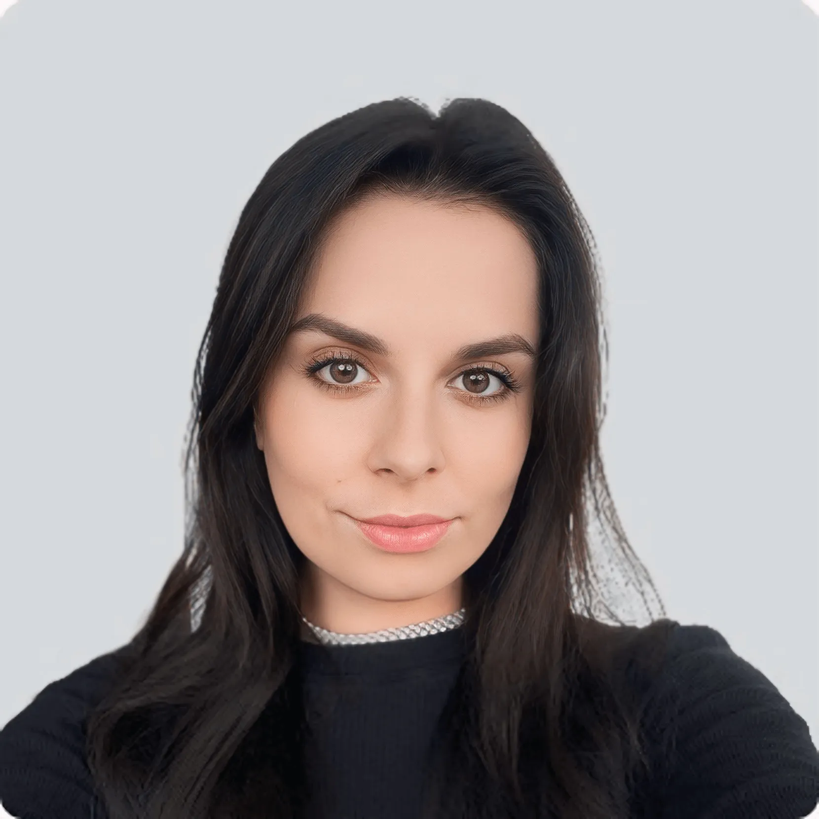 Close-up portrait of a woman with long dark hair, brown eyes, and natural makeup wearing a black top and a silver necklace, against a plain light gray background.