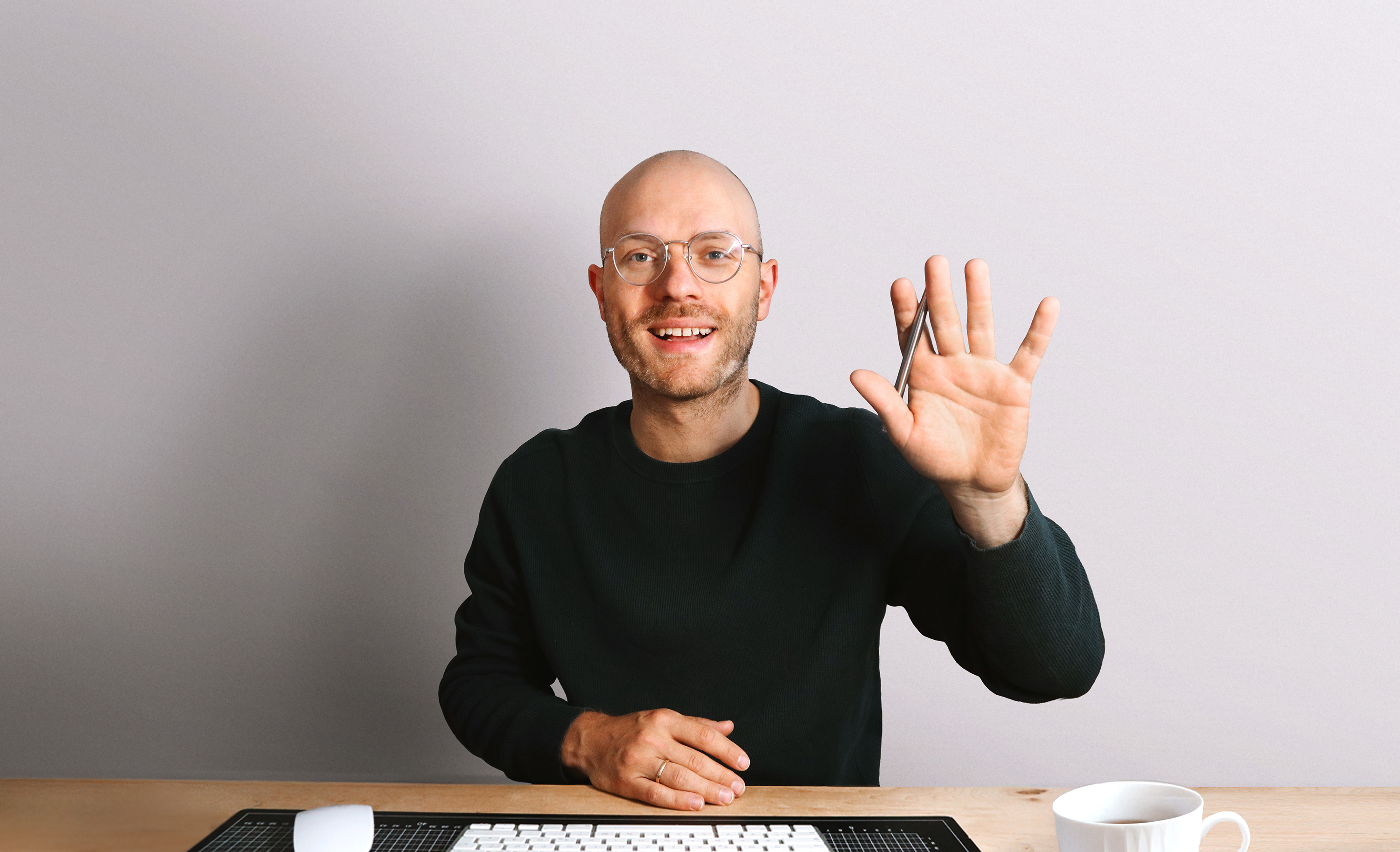 Fabian Weller, Gründer von Studio Weller, sitzt am Schreibtisch und winkt in die Kamera