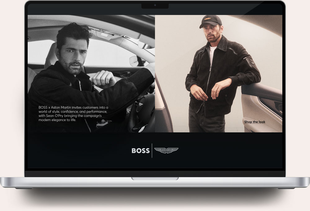 Laptop screen showing a BOSS x Aston Martin campaign with Sean O’Pry. On the left, a black-and-white photo of Sean O’Pry sitting in a car wearing a dark jacket. Text reads: BOSS x Aston Martin invites customers into a world of style, confidence, and performance, with Sean O’Pry bringing the campaign's modern elegance to life. On the right, Sean O’Pry stands next to a car door in a dark jacket and cap with the text 'Shop the look'. BOSS and Aston Martin logos appear at the bottom.