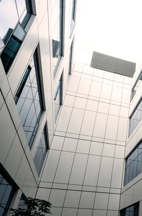 Looking up inside a modern building courtyard with reflective glass windows and white panelled walls.