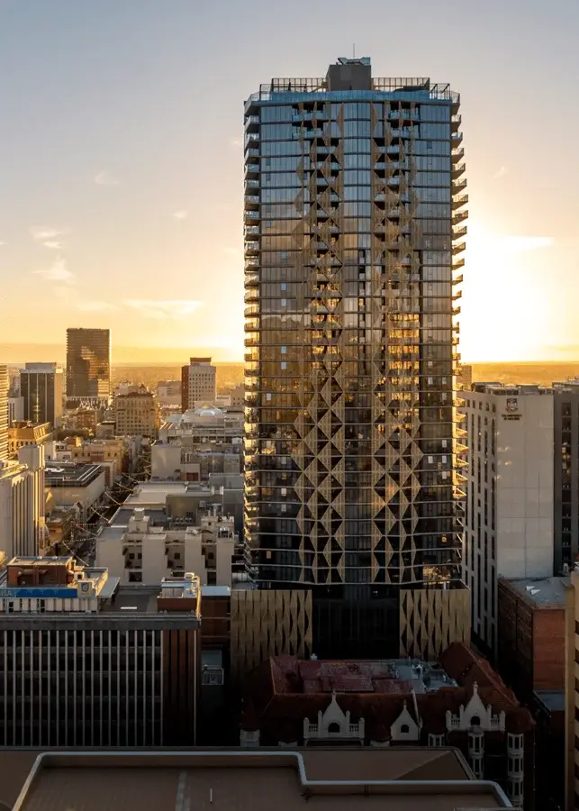 Modern glass skyscraper reflecting sunset in a city skyline.