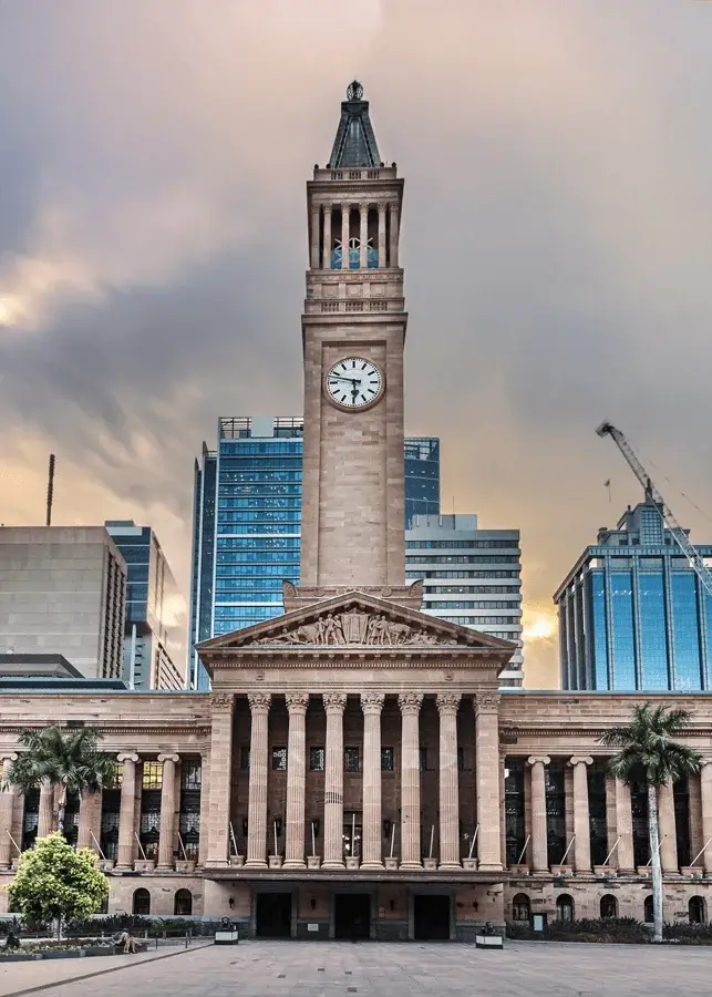 Historic Brisbane City Hall with its clock tower set against modern skyscrapers at dusk.