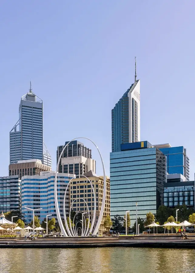 Perth city skyline featuring modern high-rise buildings and the white circular Elizabeth Quay arches sculpture by the waterfront under clear blue sky.