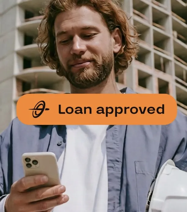 A builder on a construction site reading a loan approval on his phone