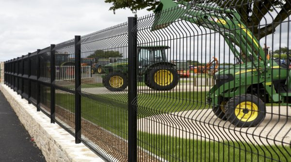 Fekete fémszerkezetű kerítés mezőgazdasági gépek, köztük traktor mellett.