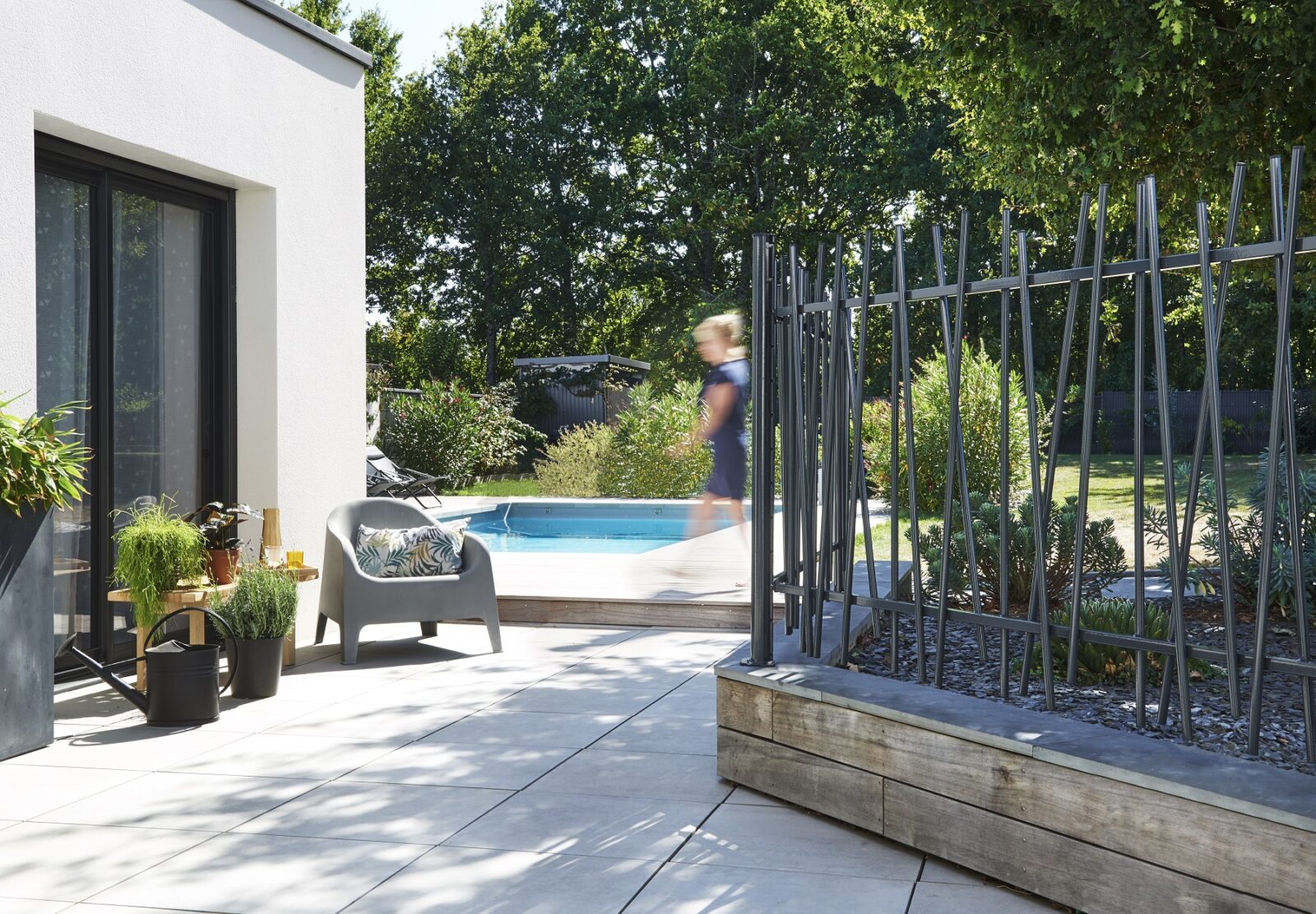 Modern patio with potted plants, a gray chair, and a small pool in a sunny garden setting.