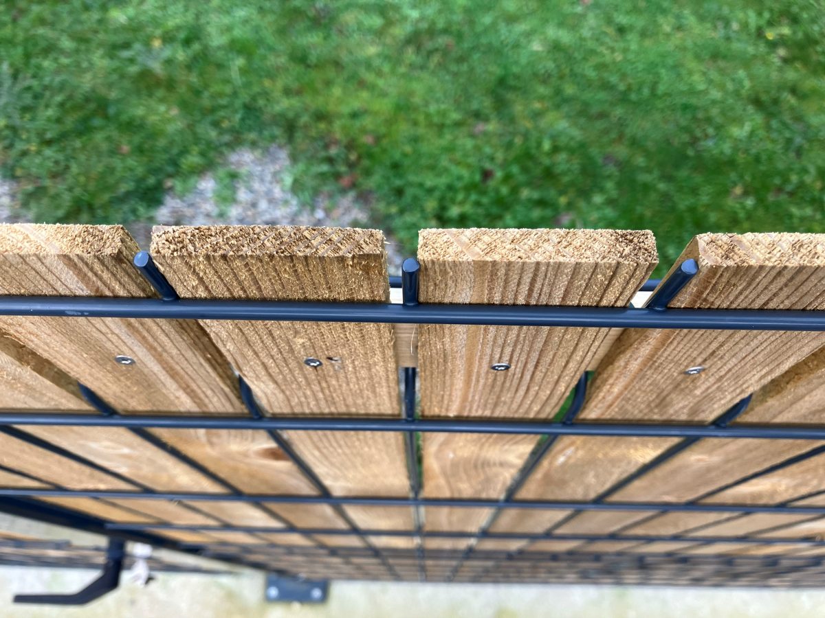 Fából és fekete fémből készült kerítés egy zöld füves terület előtt.