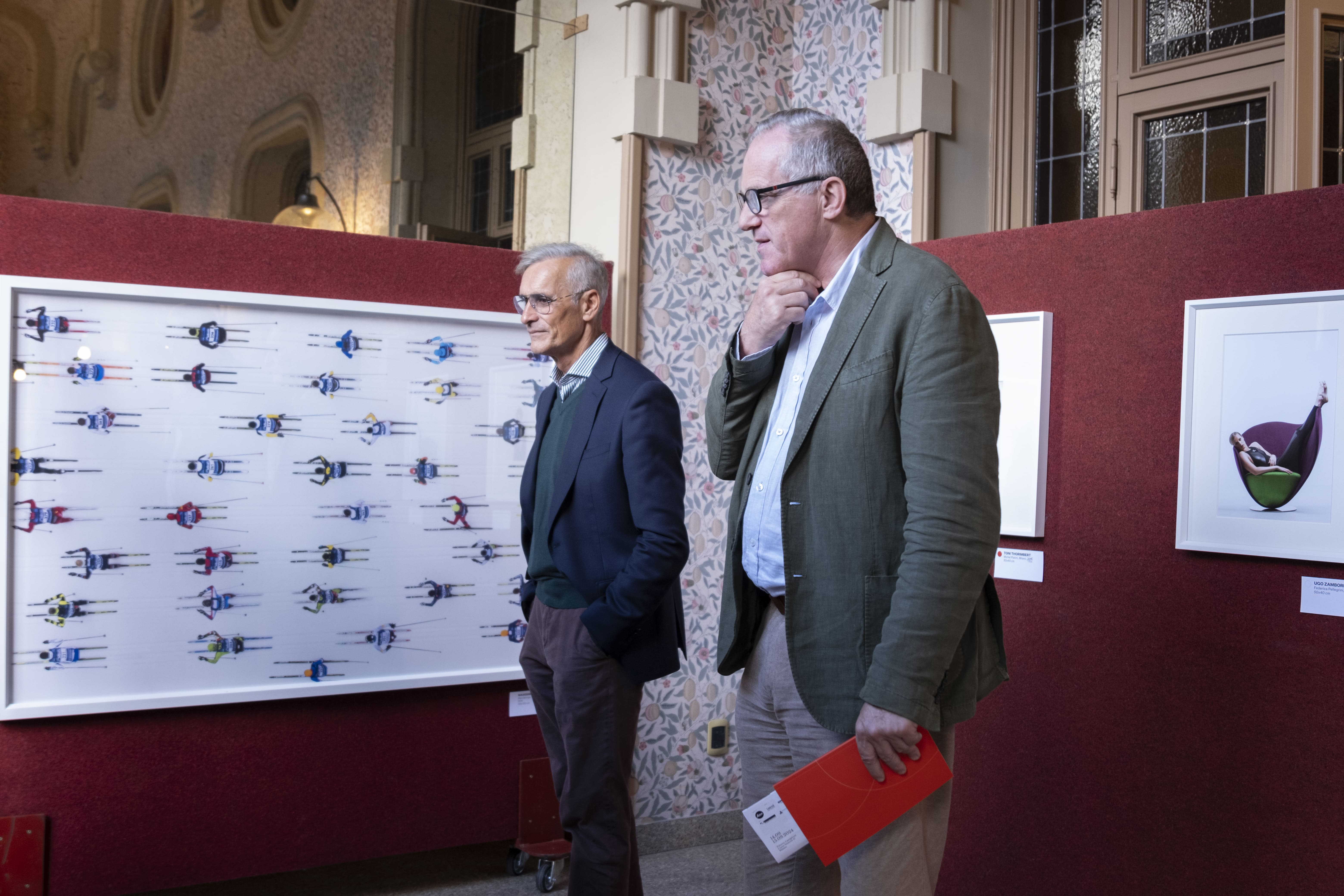 Gruppo di persone che partecipano a una corsa indossando magliette arancioni con scritte You Sport, alcune fanno il segno della vittoria e tengono uno striscione con la scritta 'Diversity is our normal'.