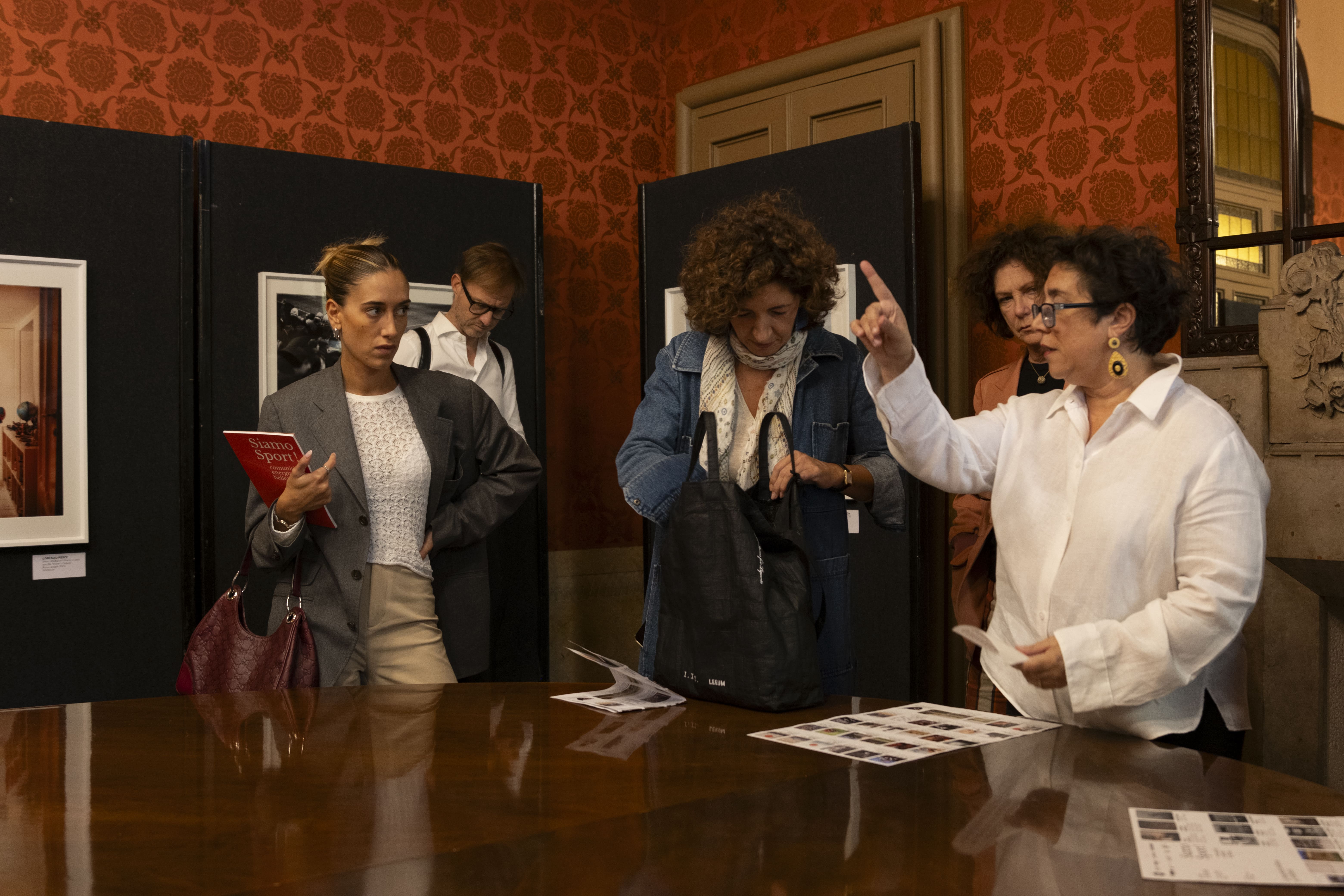 Gruppo di persone che partecipano a una corsa indossando magliette arancioni con scritte You Sport, alcune fanno il segno della vittoria e tengono uno striscione con la scritta 'Diversity is our normal'.