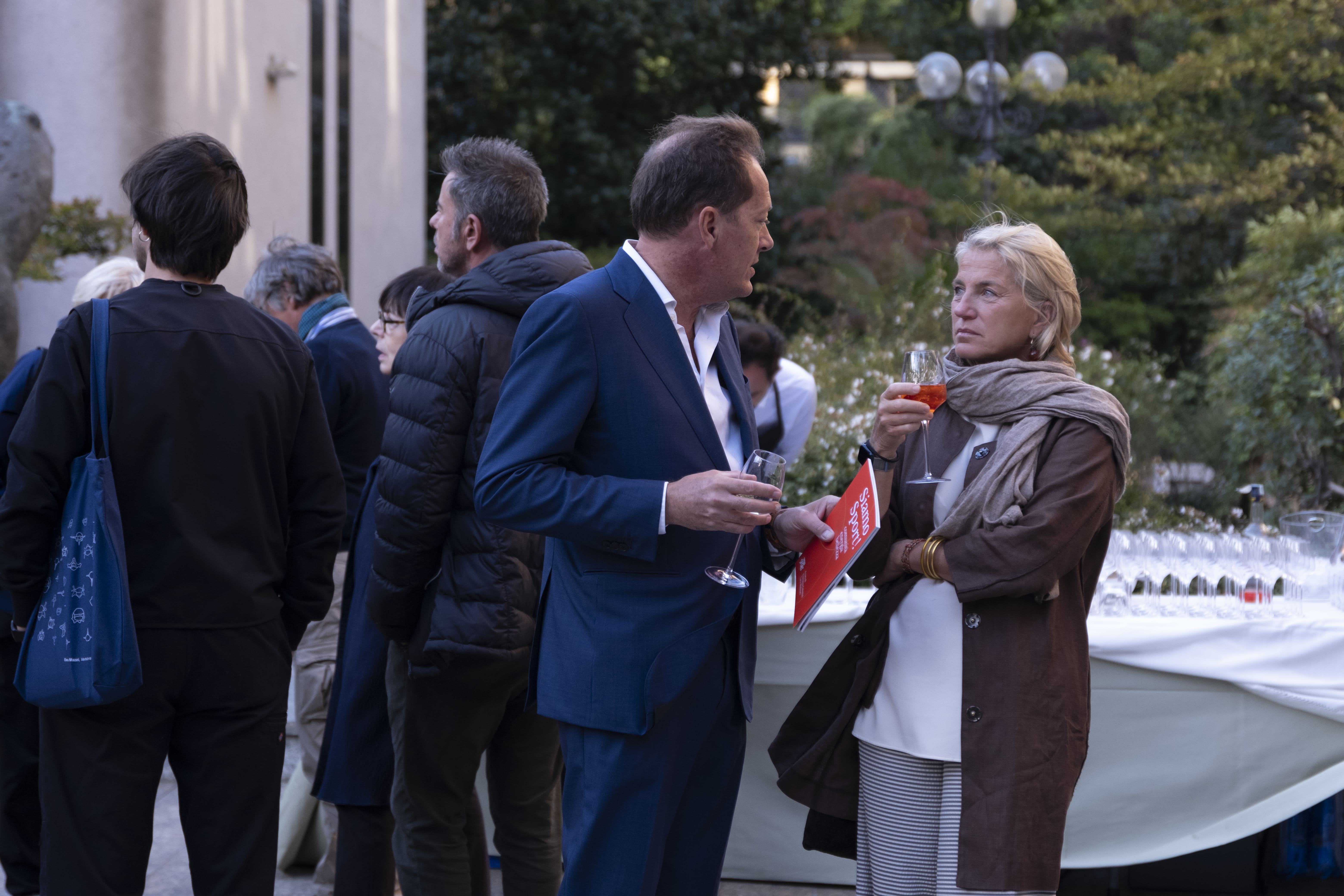 Gruppo di persone che partecipano a una corsa indossando magliette arancioni con scritte You Sport, alcune fanno il segno della vittoria e tengono uno striscione con la scritta 'Diversity is our normal'.