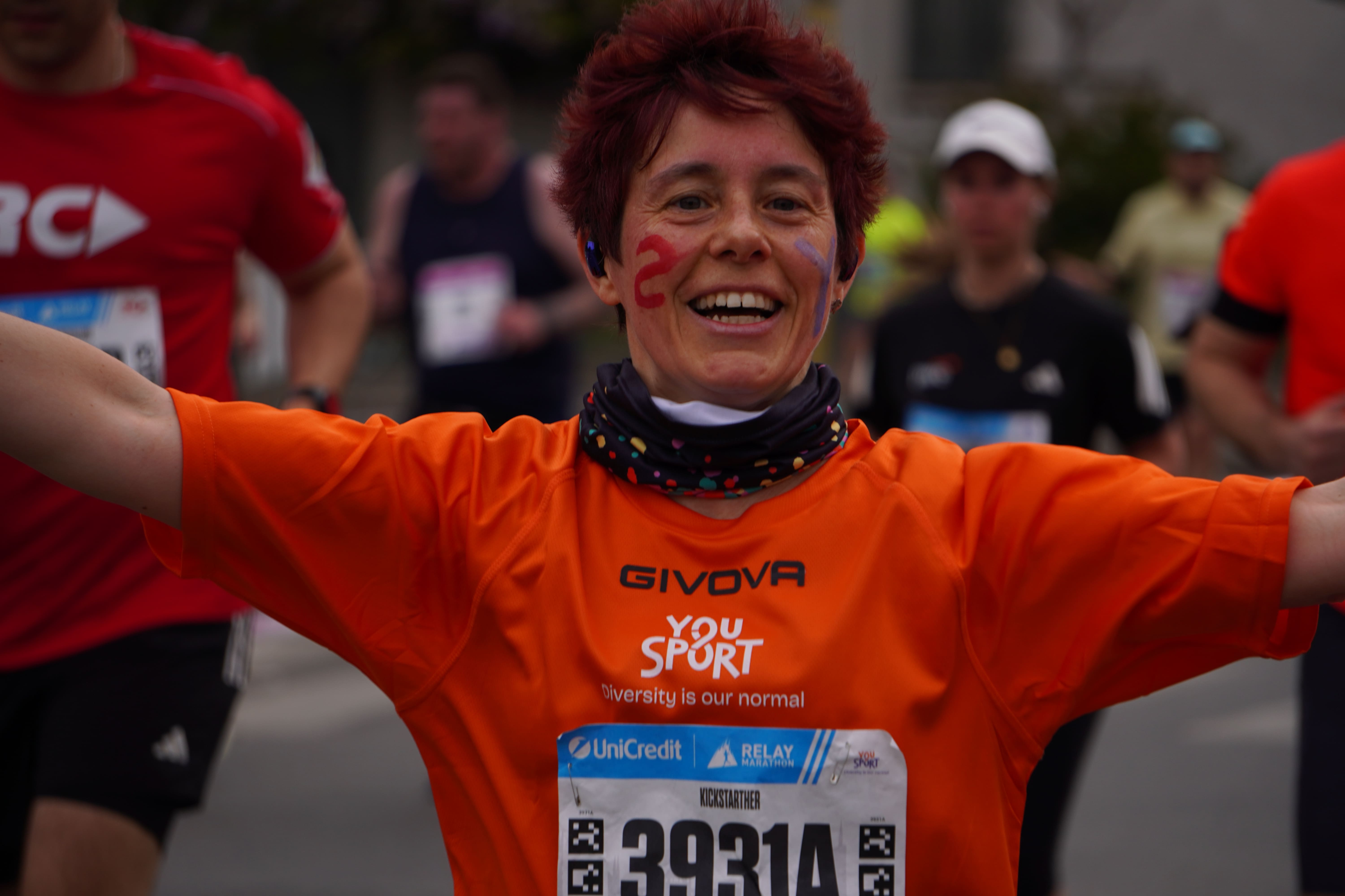 Gruppo di giovani sorridenti con medaglie, alcuni indossano magliette arancioni con la scritta YouSport, festeggiano all'aperto dopo una gara.