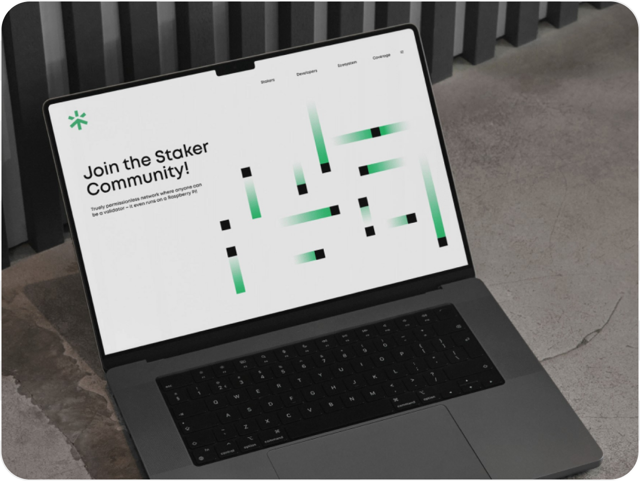 A laptop on a concrete surface displays a webpage titled "Join the Staker Community!" with green and black abstract graphics, conveying a tech-savvy vibe.