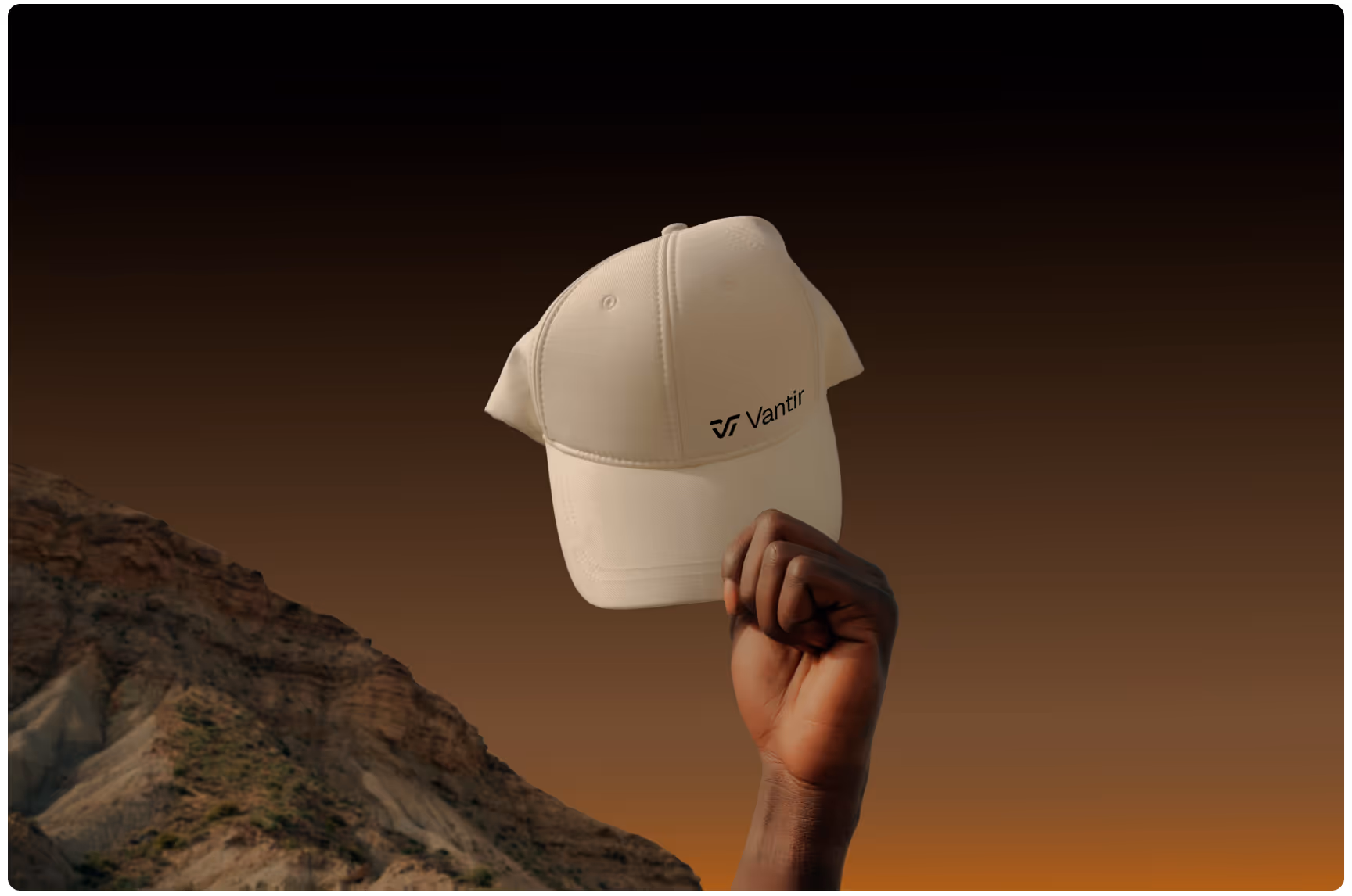 An outstretched hand holds a beige cap with "Vantir" logo, against a backdrop of dramatic rocky terrain and a warm, darkening sky, conveying adventure.