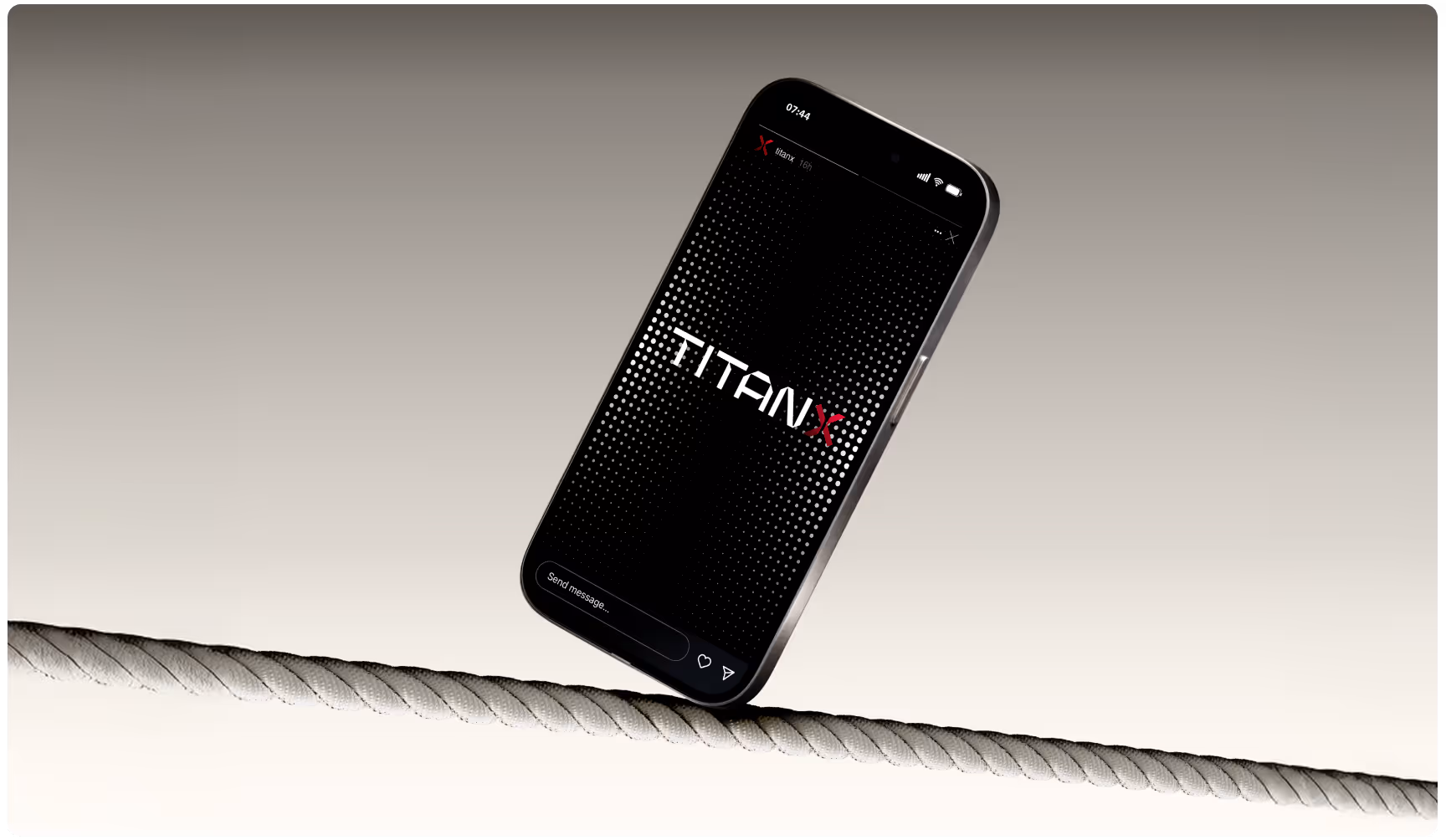 A smartphone with a black screen displaying "TITAN X" in bold, white letters, balances on a thick rope against a neutral gray background, conveying stability.
