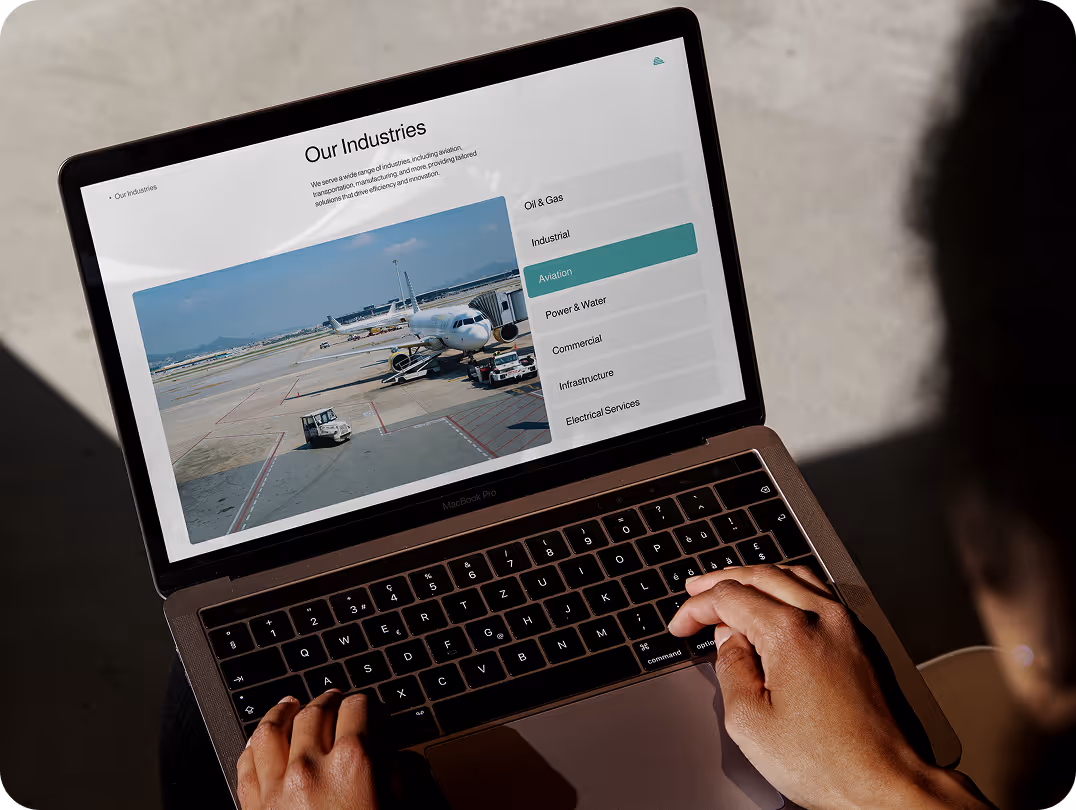 Person viewing a website on a laptop screen. The site shows "Our Industries" with a highlighted "Aviation" section and an airport image.