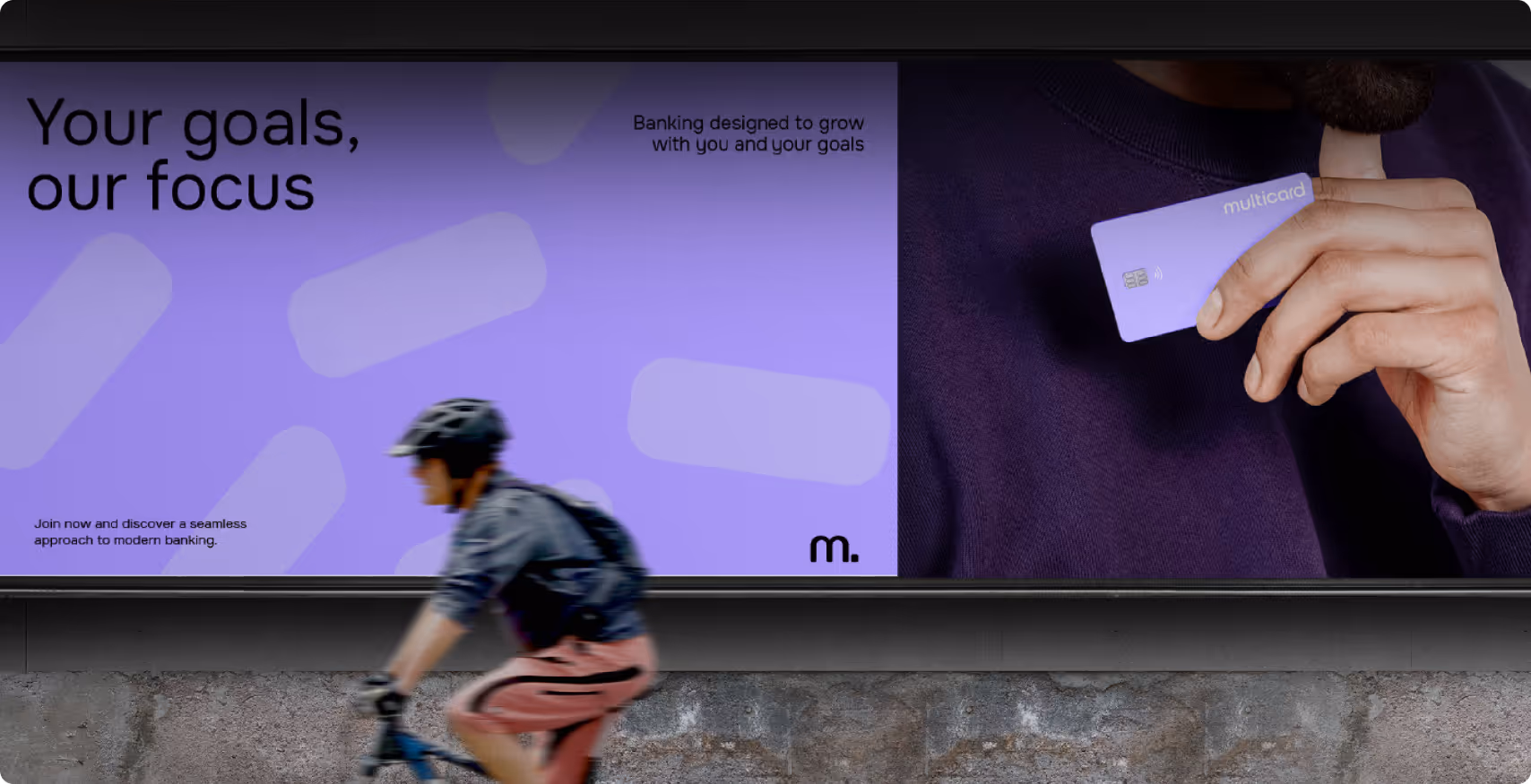 Billboard shows a person holding a purple multicard with text "Your goals, our focus" and "Banking designed to grow with you and your goals." A cyclist passes by.