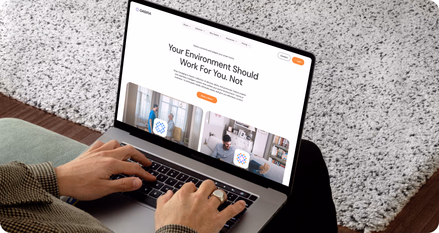 A person uses a laptop displaying a website with the headline "Your Environment Should Work For You, Not." The scene is calm, featuring a cozy room with a white rug and wooden floor.