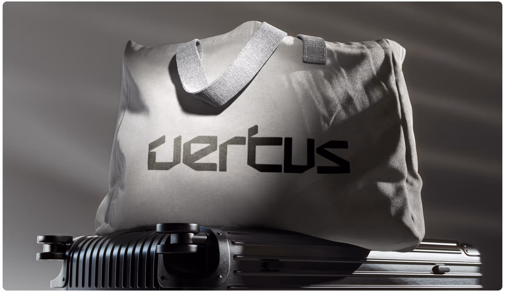 A gray canvas bag with the word "vertus" printed on it sits on top of a metallic suitcase. The lighting casts soft shadows, creating a sleek, modern feel.