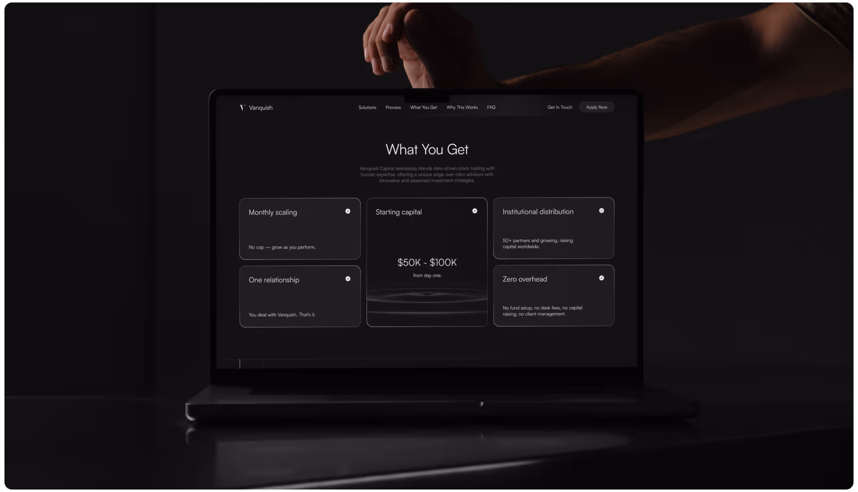 A dimly lit laptop screen displays a webpage titled "What You Get." It lists features like monthly scaling, starting capital, and zero overhead. A hand hovers above, adding a contemplative mood.