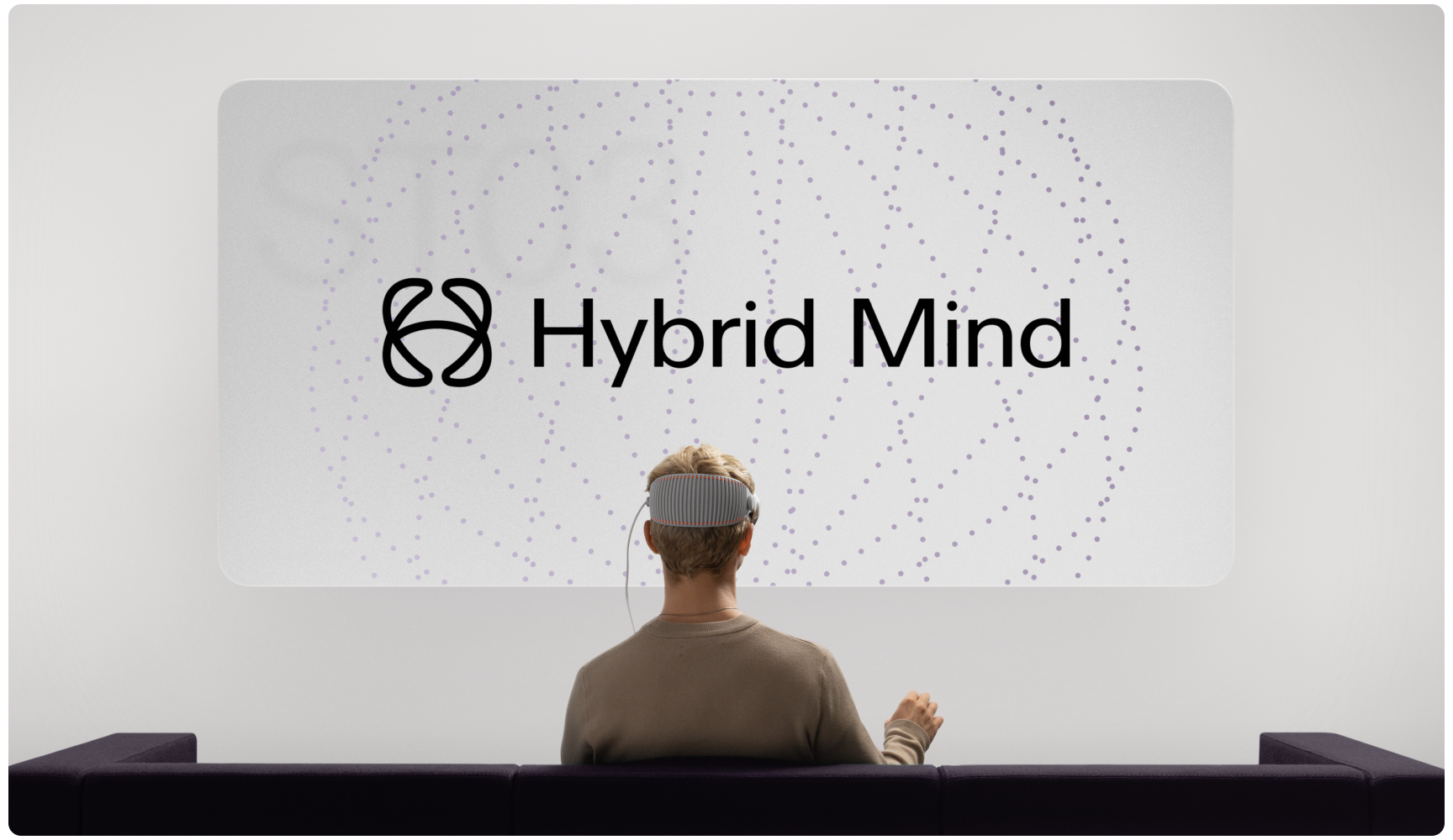 A person wearing a VR headset sits on a sofa facing a screen displaying "Hybrid Mind" with a dotted pattern. The setting is modern and tech-focused.