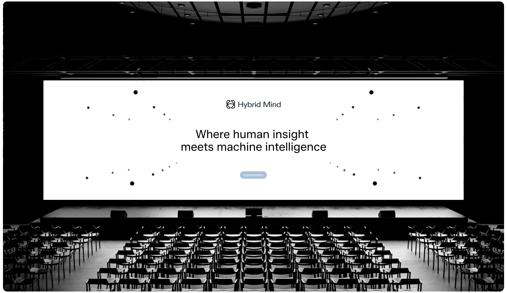 Large auditorium with rows of empty chairs facing a wide screen that reads "Hybrid Mind: Where human insight meets machine intelligence." Modern and professional atmosphere.