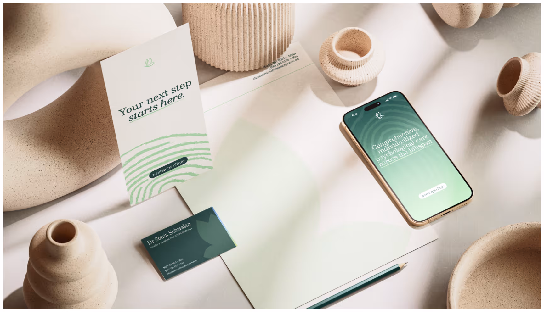 A minimalist workspace with beige ceramics. A phone displays "Congratulations!" in green; papers and a business card read "Your next step starts here."