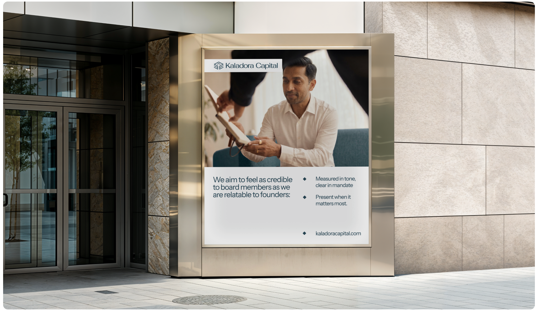 Outdoor advertisement for Kaladora Capital on a building facade. It features a professional man receiving a document, conveying trust and professionalism.