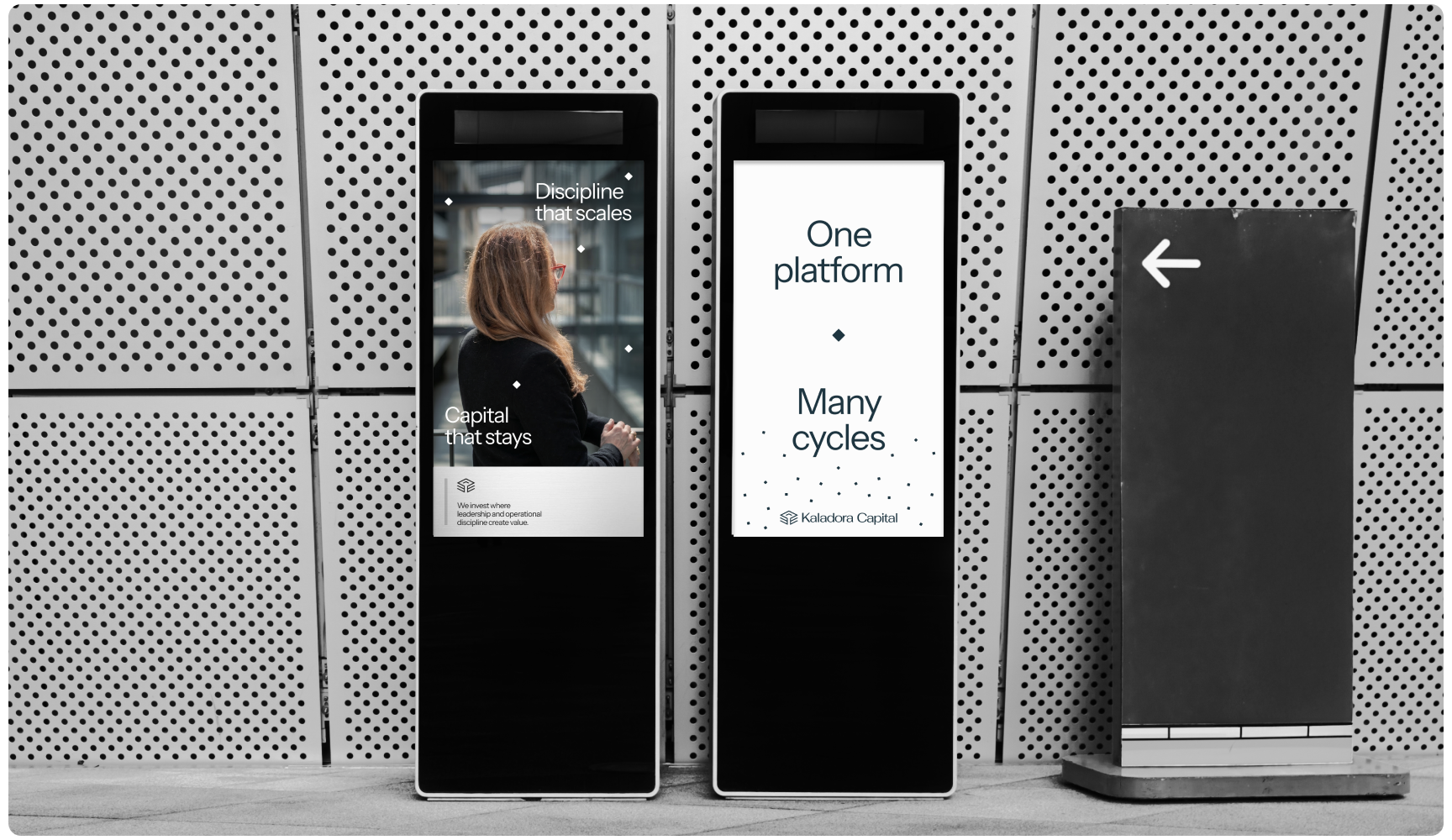 Two sleek advertising kiosks stand against a perforated metal wall. The left displays a woman with text "Discipline that scales"; the right reads "One platform, Many cycles." Minimalist design and modern feel.
