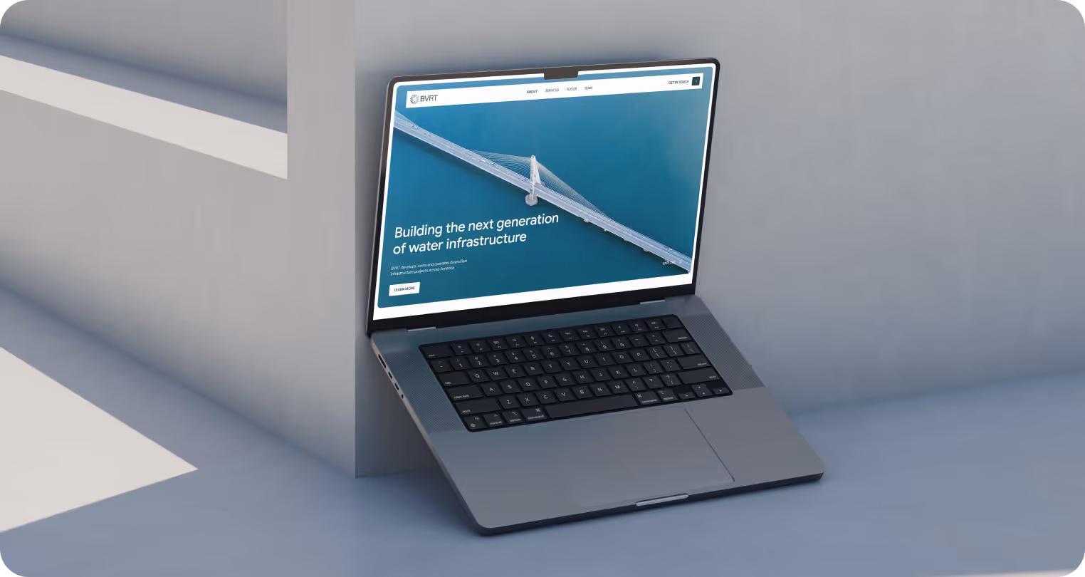 Laptop leaning against a concrete wall on a sunny day, displaying a website about water infrastructure with an aerial view of a bridge over water.