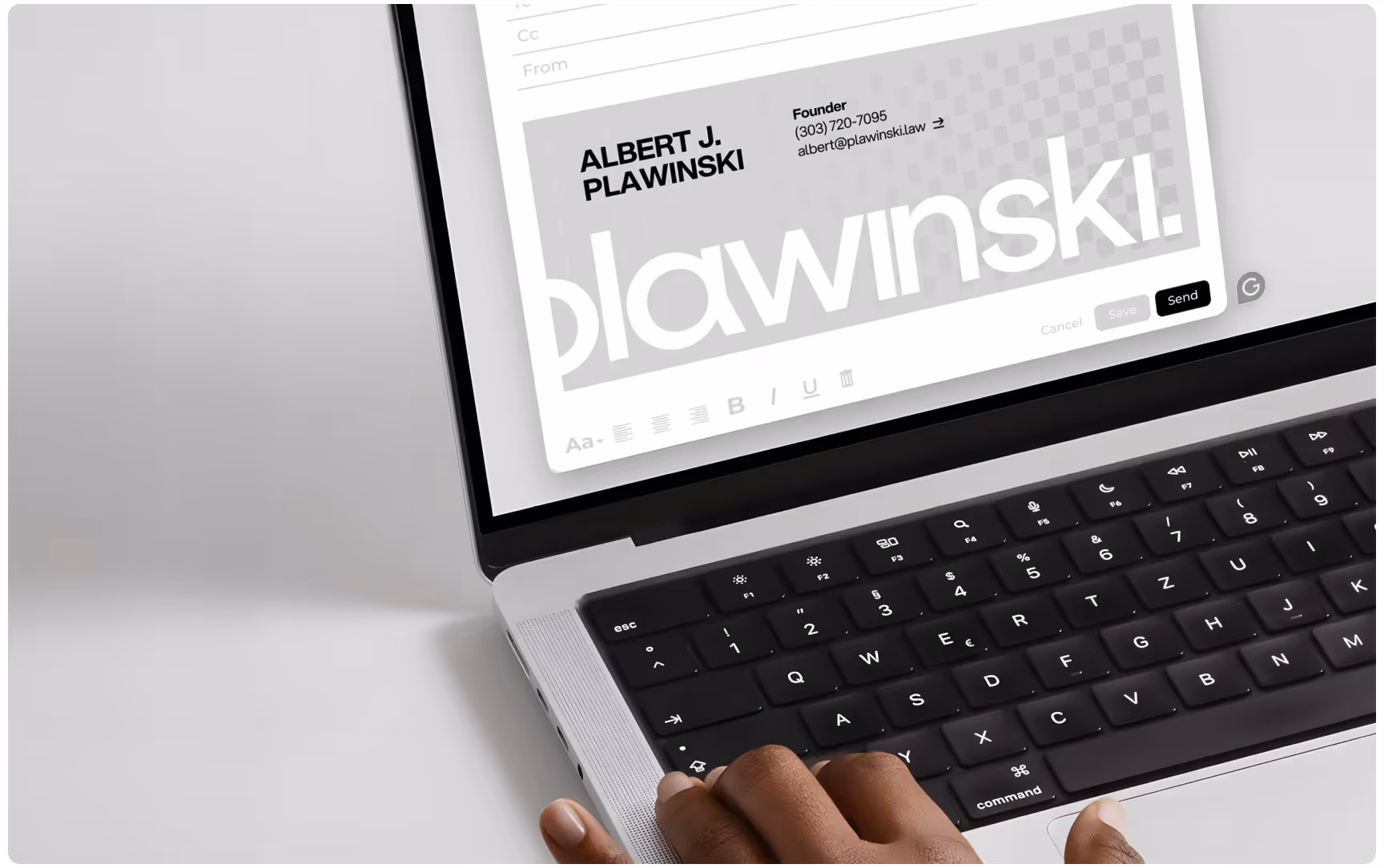 Close-up of a laptop displaying a branded Plawinski email signature design featuring bold typography, founder contact details, and minimalist grayscale graphics, with a hand resting on the keyboard in a modern workspace.