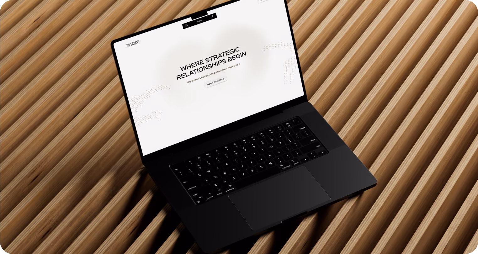 Black laptop displaying the Ledger Society website on a warm wooden slatted surface. The screen features the headline “WHERE STRATEGIC RELATIONSHIPS BEGIN” with minimalist white branding and subtle dotted graphics.