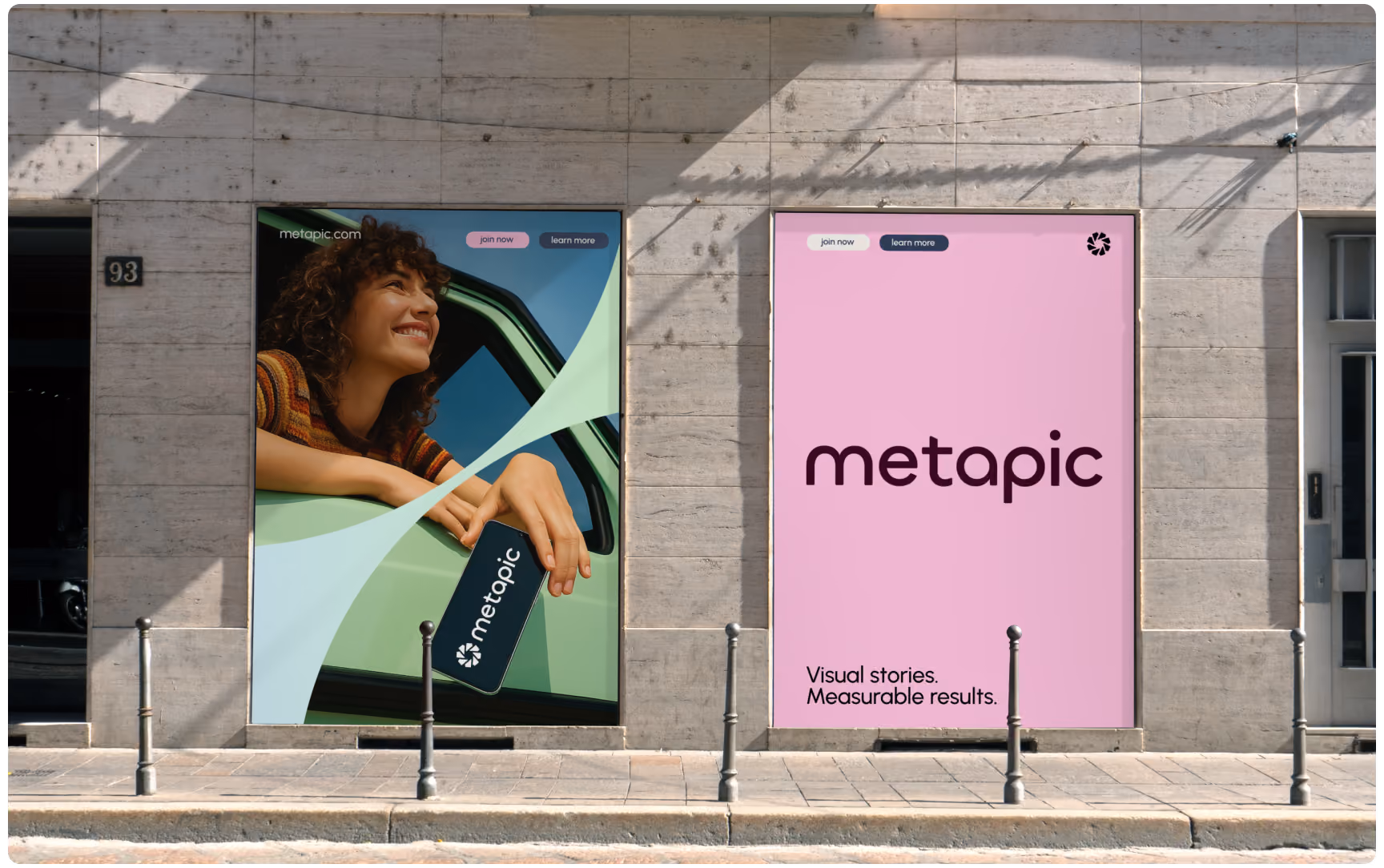 Two street-level Metapic posters side-by-side on a stone building wall, one showing a woman leaning out of a car window holding a smartphone, and the other displaying the tagline "Visual stories. Measurable results." on a pink background.