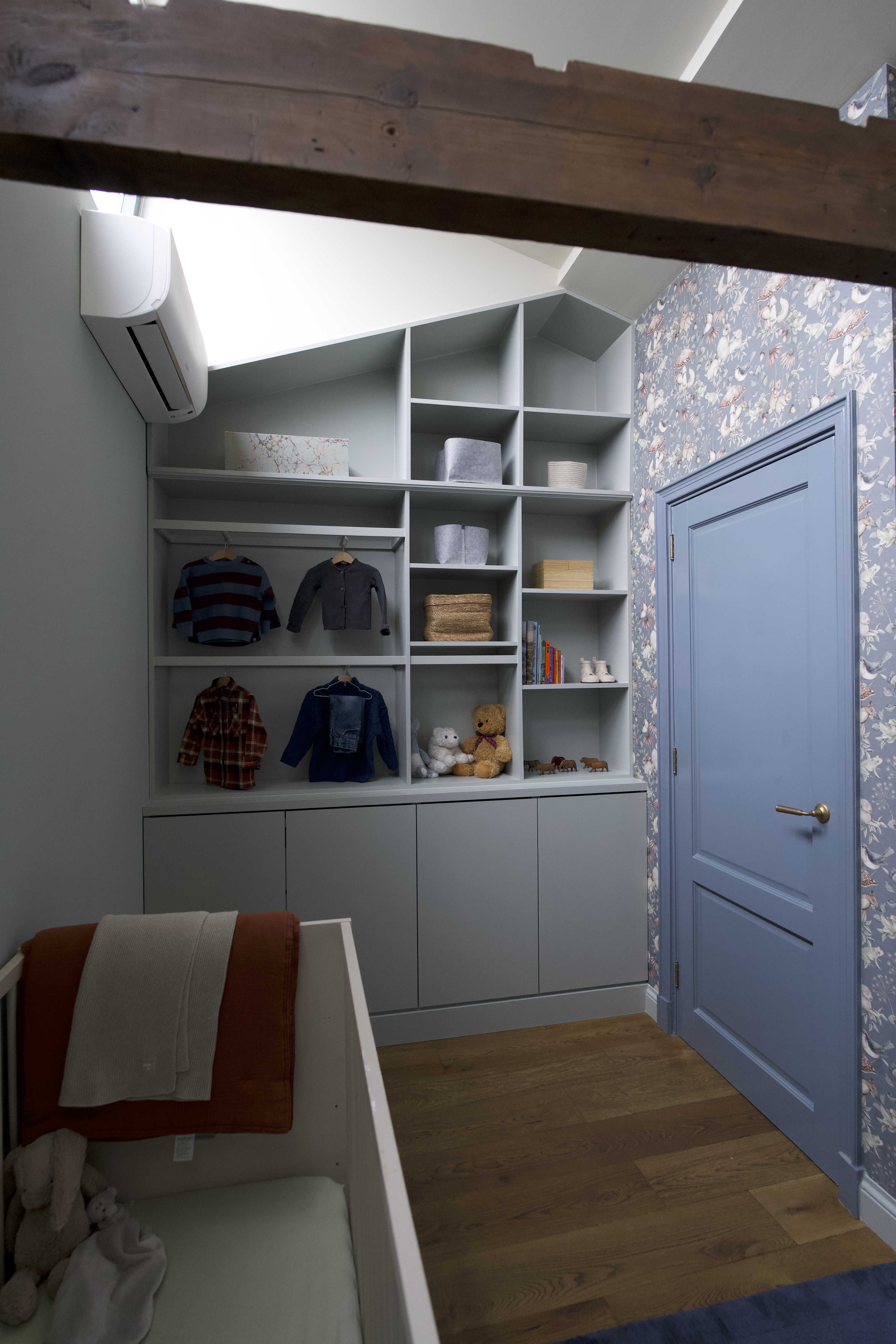 Custom light grey nursery wardrobe with open shelving for children's clothes and toys, next to a blue door