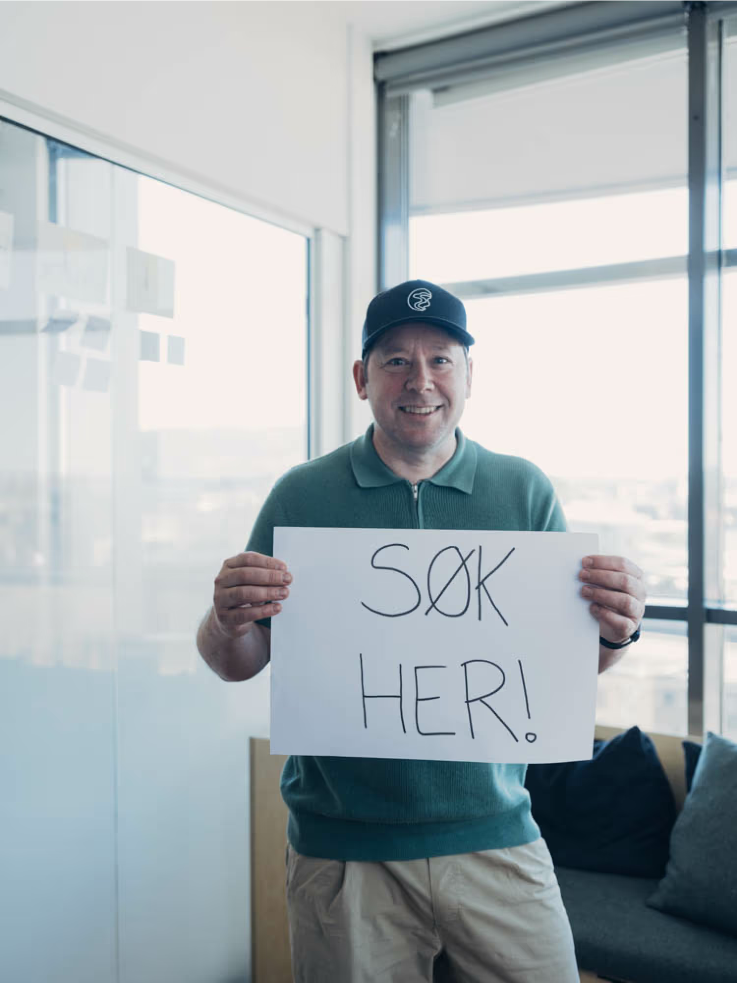 Man holding a sign that says 'Søk her!' (Apply here!) at Capra.