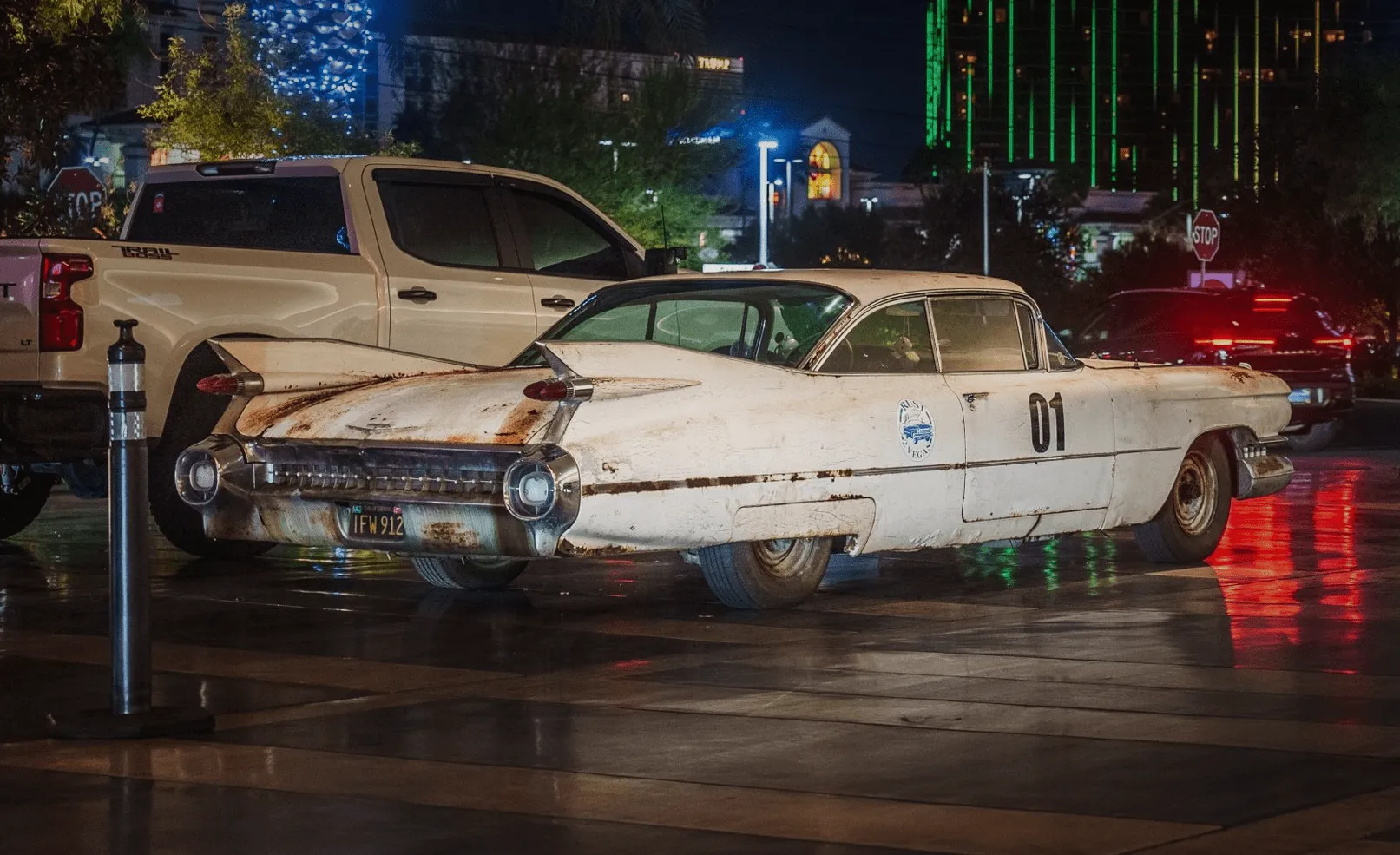 Rusty white vintage Cadillac with number 01 on the door parked at night under city lights.