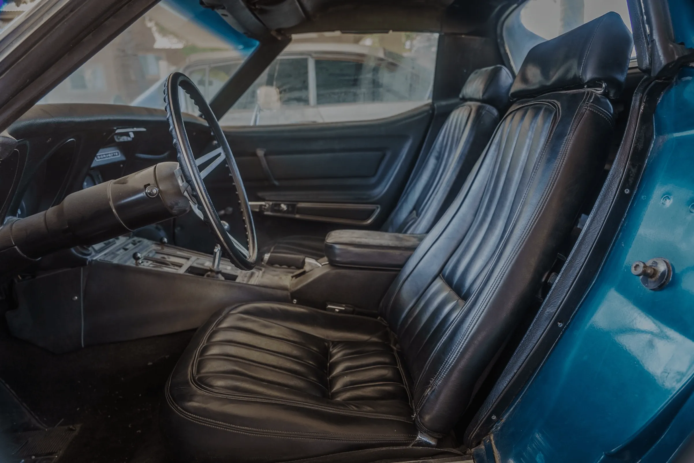 Interior of a classic Corvette showing black leather seats, steering wheel, and dashboard.