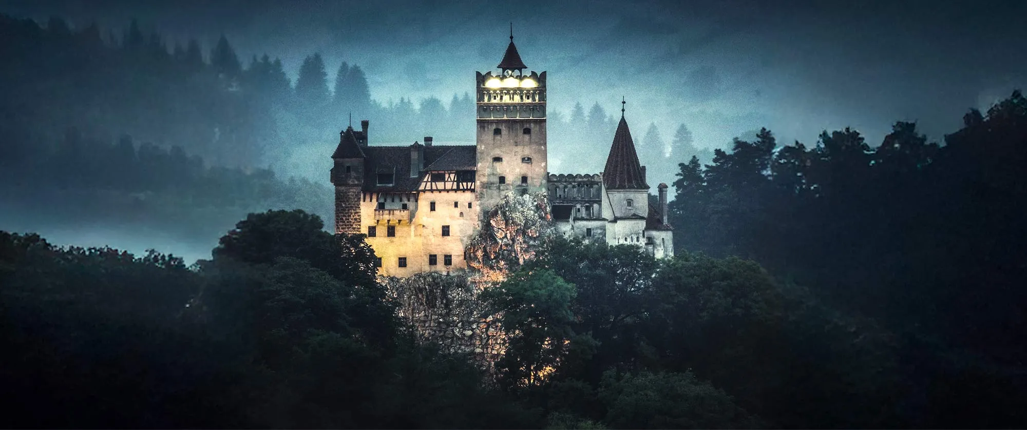 A dramatic, illuminated castle surrounded by dense forest and misty hills at dusk, with a dark and mysterious atmosphere.