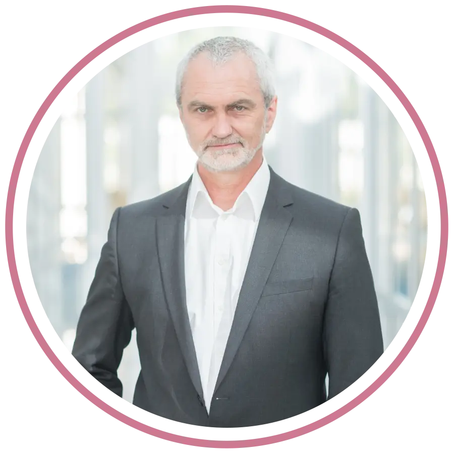 „Porträtfoto von Cassandra Schwerter, Gründerin von Sent4Souls - CSG Projects, mit pink-violetten Haaren und schwarzer Bluse. Sie steht auf einer Dachterrasse vor moderner Architektur, lehnt sich lächelnd an ein Geländer.