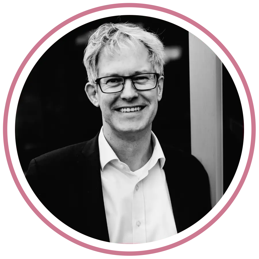 „Porträtfoto von Cassandra Schwerter, Gründerin von Sent4Souls - CSG Projects, mit pink-violetten Haaren und schwarzer Bluse. Sie steht auf einer Dachterrasse vor moderner Architektur, lehnt sich lächelnd an ein Geländer.