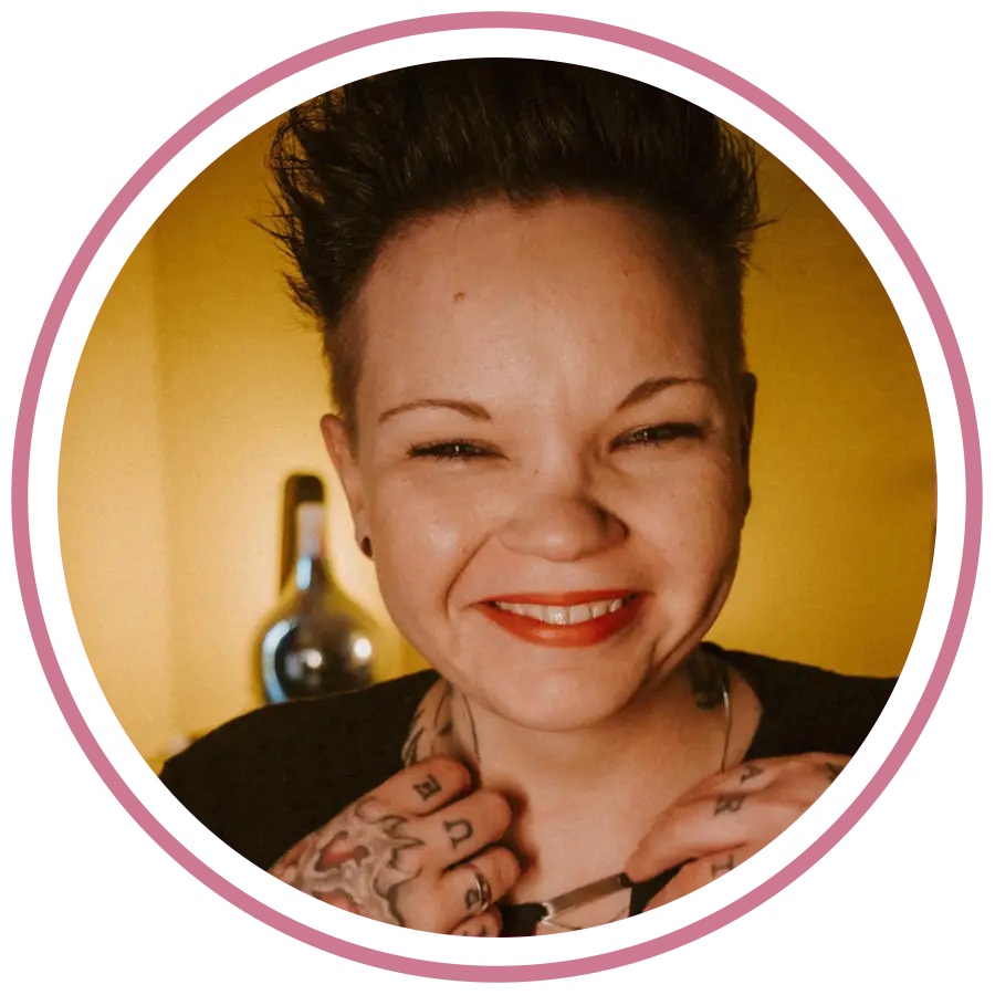 „Porträtfoto von Cassandra Schwerter, Gründerin von Sent4Souls - CSG Projects, mit pink-violetten Haaren und schwarzer Bluse. Sie steht auf einer Dachterrasse vor moderner Architektur, lehnt sich lächelnd an ein Geländer.